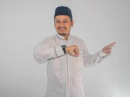 Moslem Asian man smiling and pointing to the right side while showing his watch photo