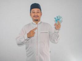 Adult Muslim Asian man smiling and showing confident when pointing to paper money that he hold photo