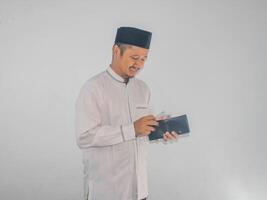 Side view of Moslem Asian man smiling happy when taking money from inside his wallet photo