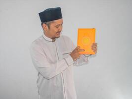 Moslem Asian man smiling while pointing to a book that he hold photo