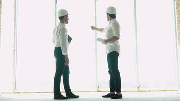 Two engineer with a drawing in hand looking at the construction site. View from the back. Chief Engineer with blueprint in hand looking at the construction video