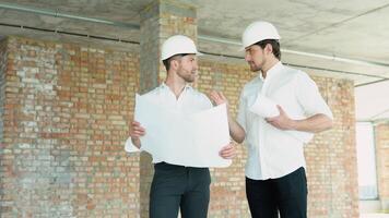 uma jovem engenheiros dentro segurança capacetes em pé em a em construção construção segurando uma projeto do a estrutura e trabalhando juntos video