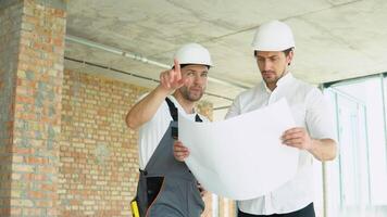 Due giovane ingegnere nel un' sicurezza caschi in piedi a edificio luogo Tenere un' planimetria di il struttura. costruzione attività commerciale. lavoro di squadra concetto video