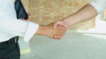 Close up of handshake in construction site. Employee or worker shake hands to employer man for greeting, dealing, collaboration project or business video