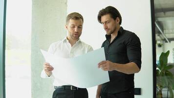 Two businessman engineers working in bright clean office. Discussing the construction project, plan, drawing, scheme video