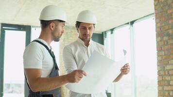 Two young engineer in a safety helmets standing at building site holding a blueprint of the structure. Construction Business. Teamwork concept video