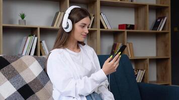 relajante hora con música. hermosa joven mujer sentado en el casa escoger música y tomar un descanso y escuchando canción con inalámbrico auricular. estilo de vida en vivo habitación a casa en el Mañana video