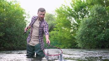 Fischer mit Angeln Stange auf das Fluss. fliegen Angeln zum Forelle. braun Forelle Fisch. Forelle auf ein Haken. halten Forelle Fisch video