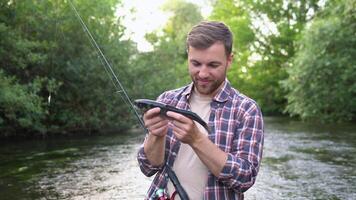 Fisherman rests on the river and catches trout, smiles and shows the fish in the camera video