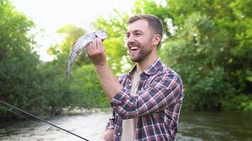 visser rust Aan de rivier- en vangsten forel, glimlacht en shows de vis in de camera. forel vissen. visvangst Aan de rivier- video