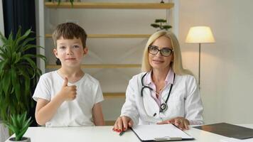 souriant Sénior femelle famille médecin dans uniforme consultant peu enfant patient à vérification réunion dans clinique video