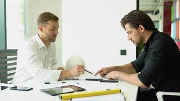 Two businessman engineers working in bright clean office. Discussing the construction project, plan, drawing, scheme video