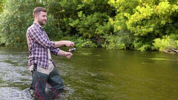 A fisherman throws a fishing rod standing knee-deep in the water of the river. Fly fishing for trout. Summer holidays and people concept video