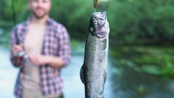 Fischer ruht auf das Fluss und fängt Forelle, lächelt und zeigt an das Fisch im das Kamera video