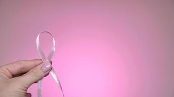 Pink symbolic ribbon in hands, symbol. World Breast Cancer Day. Close-up, isolated, pink neon background , professional lighting. video