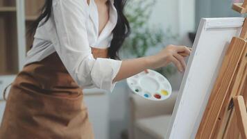 Over the shoulder selective focus shot of male artist using brush while adding color paint to pencil drawing on canvas video