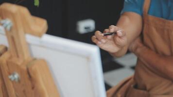 Over the shoulder selective focus shot of male artist using brush while adding color paint to pencil drawing on canvas video