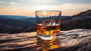 whisky con hielo en parte superior de un montaña a puesta de sol. foto