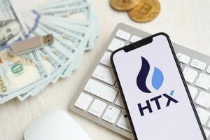 KYIV, UKRAINE - MARCH 15, 2024 HTX logo on iPhone display screen on white keyboard with money and bitcoins photo