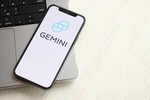 KYIV, UKRAINE - MARCH 15, 2024 Gemini logo on iPhone display screen on MacBook panel logo on iPhone display screen with dollars and bitcoins on MacBook photo