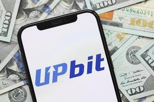 KYIV, UKRAINE - MARCH 15, 2024 Upbit logo on iPhone display screen with many hundred dollar bills photo