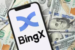 KYIV, UKRAINE - MARCH 15, 2024 BingX logo on iPhone display screen with many hundred dollar bills photo