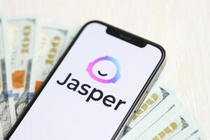 KYIV, UKRAINE - MARCH 17, 2024 Jasper logo on iPhone display screen with many hundred dollar bills photo