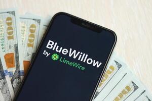 KYIV, UKRAINE - MARCH 17, 2024 BlueWillow logo on iPhone display screen with many hundred dollar bills photo