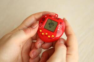 KYIV, UKRAINE - MARCH 9, 2024 Retro pet keychain game tamagotchi in red plastic case in female hands photo