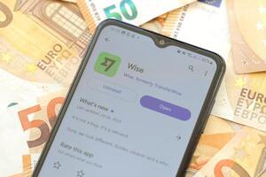 TERNOPIL, UKRAINE - AUGUST 3, 2023 Wise application on screen on modern smartphone and many bills of euro currency photo