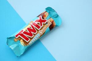 TERNOPIL, UKRAINE - JULY 7, 2023 Twix salted caramel blue wrapper on wooden background. Twix is a chocolate bar made by Mars Inc consisting of biscuit applied with caramel photo