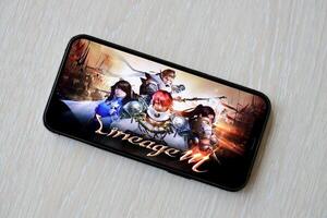 Lineage M mobile iOS game on iPhone 15 smartphone screen on wooden table during mobile gameplay photo
