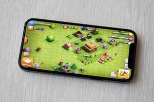 Clash of Clans mobile iOS game on iPhone 15 smartphone screen on wooden table during mobile gameplay photo