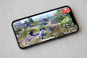 PUBG PlayerUnknowns Battlegrounds mobile iOS game on iPhone 15 smartphone screen on wooden table during mobile gameplay photo