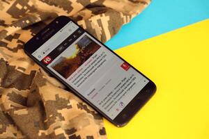 KYIV, UKRAINE - 4 MAY, 2023 NV ukrainian news portal on smartphone screen with ukrainian flag and camouflage fabric photo