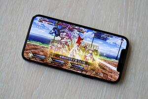 Fate Grand Order mobile iOS game on iPhone 15 smartphone screen on wooden table during mobile gameplay photo