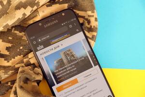 KYIV, UKRAINE - 4 MAY, 2023 Unian ukrainian news portal on smartphone screen with ukrainian flag and camouflage fabric photo