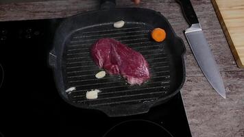 Sliced carrots and garlic are added to a piece of raw beef that has just started to cook in a frying pan with boiling oil. Cooking lesson. Close up. Slow motion. Top view video