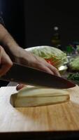 Cook cuts the zucchini, which has been peeled, into slices. This happens in the restaurant's kitchen, along with other vegetables, for the ratatouille recipe. Vertical. Close up. 4k. video