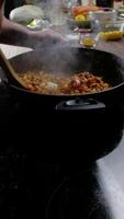 maíz, garbanzos, y rojo frijoles son conjunto con un de madera cuchara en un fritura cacerola, en contra el fondo de otro ingredientes en el mesa. el apetitoso aroma de el plato sube desde el cacerola. vertical. cerca arriba. 4k alto ángulo video