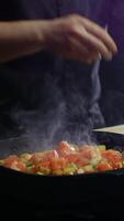 cook adds red, juicy tomato slices to a frying pan where colorful vegetables are already cooking. Vertical. Close up. 4k. video