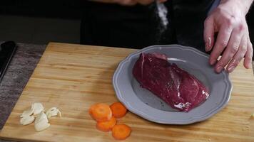 Chef seasoned a piece of raw meat with salt and then flipped it over on a plate to coat it in oil. Close up. Slow motion. High angle. video