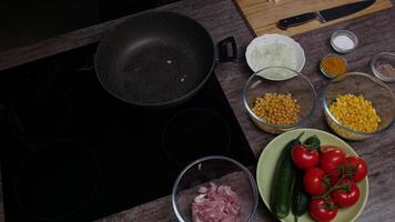 Hot frying pan is filled with vegetable oil and then raw onions are added. All this is done while surrounded by fresh, ripe vegetables and raw meat, ready for cooking. Top view . Close up. 4k. video