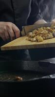 Cook places the chopped chicken meat from the cutting board in a preheated frying pan to cook it in the traditional Turkish doner style. Vertical. Close up. 4k. video