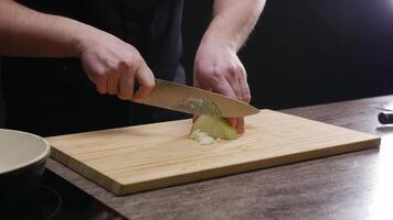 The cook skillfully and deftly cuts an onion on the cutting board. It is so ripe and juicy that drops of juice splash from it. Mid shot. 4k. High angle. video