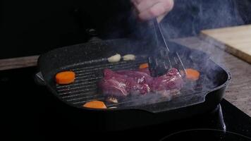 cuisinier soigneusement flips une juteux, délicieux du boeuf steak dans le friture poêle. le cuisine pétrole grésille et éclaboussures dans tout directions comme il cuisiniers. proche en haut. lent mouvement. haute angle. video