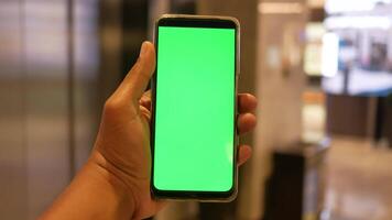 Holding slim telefoon met groen scherm tegen boodschappen doen winkelcentrum achtergrond video