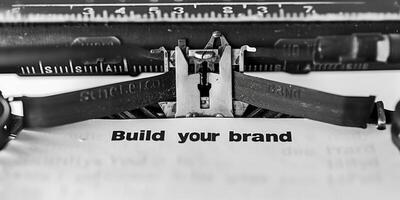 A black and white photo of the text Build your brand written on paper with an old typewriter