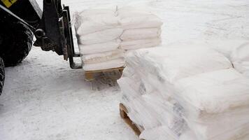 A forklift is loading large sacks of starch into a warehouse. Forklift in the winter on the street. In winter, a loader loads sacks of sugar on the street. Loader loads bags of sugar. photo