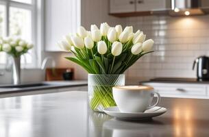 Beautiful fresh spring flowers white tulips bouquet in glass vasewith cup mug of coffee latte cappuccino in light contemporary kitchen interrior photo